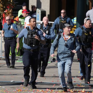 Uniformed officers, with guns drawn, run to the scene of a shooting at a parade in Kansas City. 