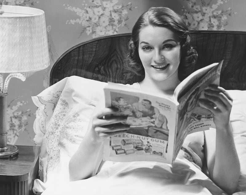 50s woman in bed, reading magazine