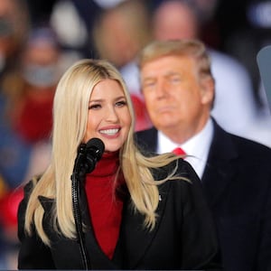 Ivanka Trump smiles at a podium in front of a blurred out Donald Trump and his supporters