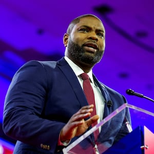 Byron Donalds speaks on stage at CPAC, wearing a suit and tie.