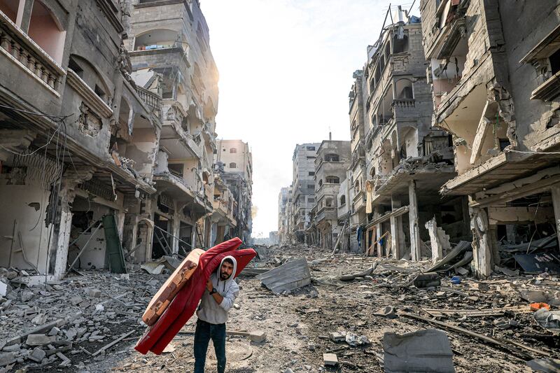 A man walks with a mattress through destruction in a Gaza Strip refugee camp