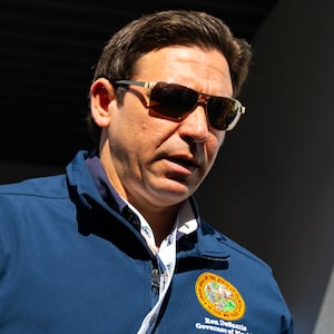 Ron DeSantis, wearing sunglasses, walks through a doorway while looking down.