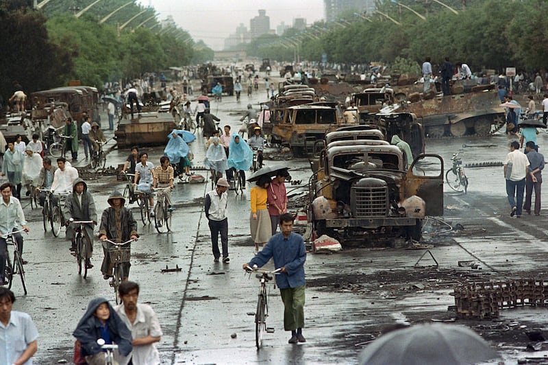 Burnt vehicles and people are scattered around a street.