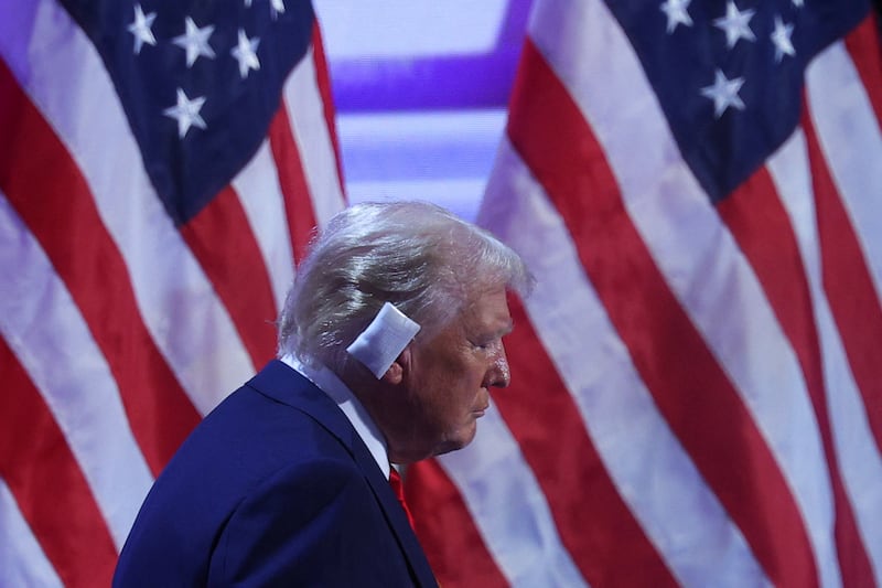 Donald Trump exits the stage with a backdrop of American flags and a bandage over his right ear.