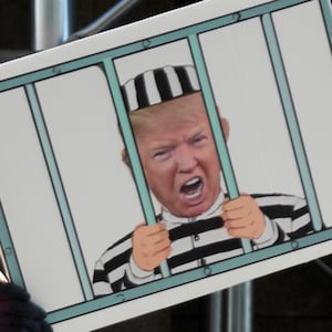 A protester holding a sign with a photo of Trump behind bars.