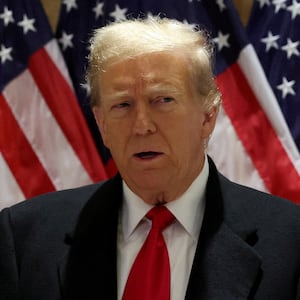 Donald Trump stands in front of American flags.