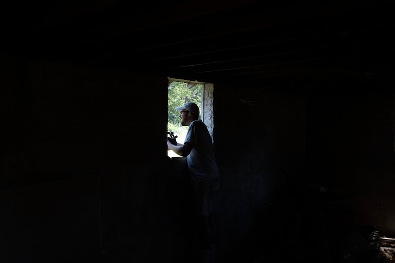 John Wilson stands in a dark house with a video camera.