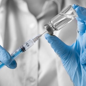 white coat lab technician with blue gloves holding flu shot universal influenza vaccine jab