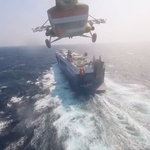 A helicopter descending toward a cargo ship at sea.