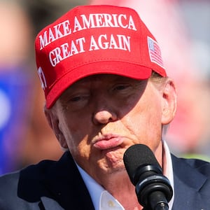 Donald Trump purses his lips while raising his hand on stage at a campaign rally.