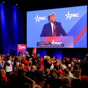 A monitor shows Donald Trump speaking at CPAC as supporters in the crowd cheer