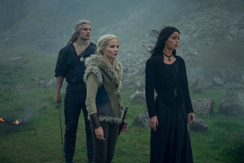 Henry Cavill, Freya Allan, and Anya Chalotra stand in a field from a scene in the third season of The Witcher.