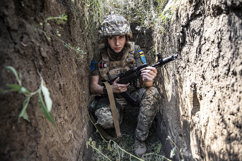 A photo a Ukrainian women soldier sitting in a trench with a rifle in 2022.