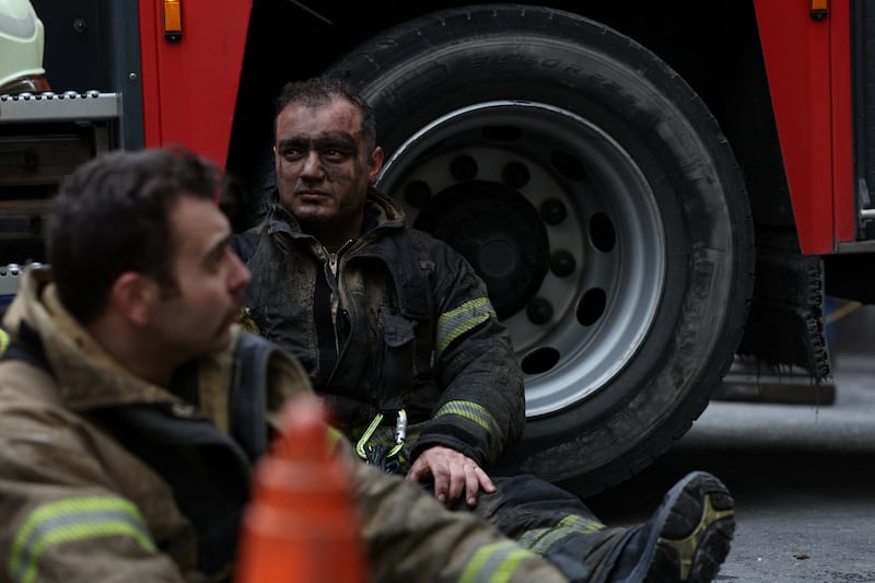 A firefighter sits down in uniform with his face blackened after fighting a fire.