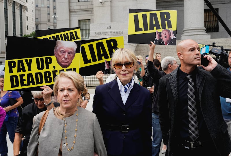 E. Jean Carroll in front of signs showing pictures of Donald Trump and saying Liar 