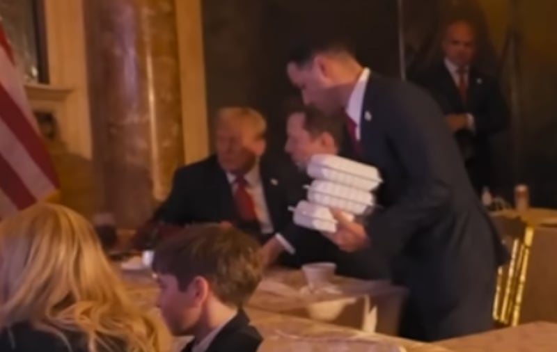 A closeup of a still from a YouTube video posted by Kai Trump shows her grandfather with what appears to be a glass of cola as an aide delivers takeout food.