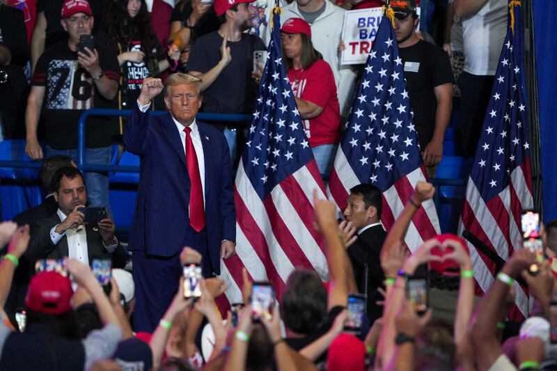 Donald Trump holds up his fist while rally-goers applaud him.