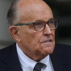 Rudy Giuliani, wearing glasses and a suit, looks forward as he leaves a federal courthouse.