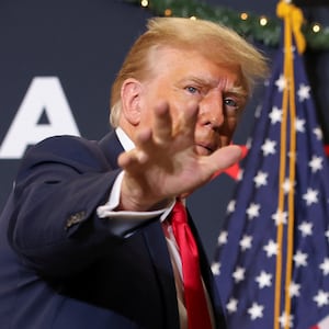 Former President Donald Trump waves at a campaign event before a flag.