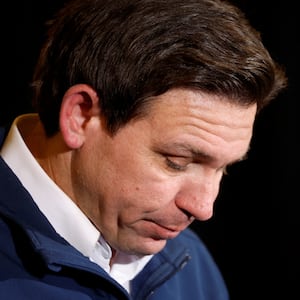 Ron DeSantis, wearing a zip-up sweater over a collared shirt, looks down as he hosts a campaign event.