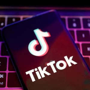 A TikTok logo is displayed on a phone screen, which is sitting on top of a laptop’s keyboard.