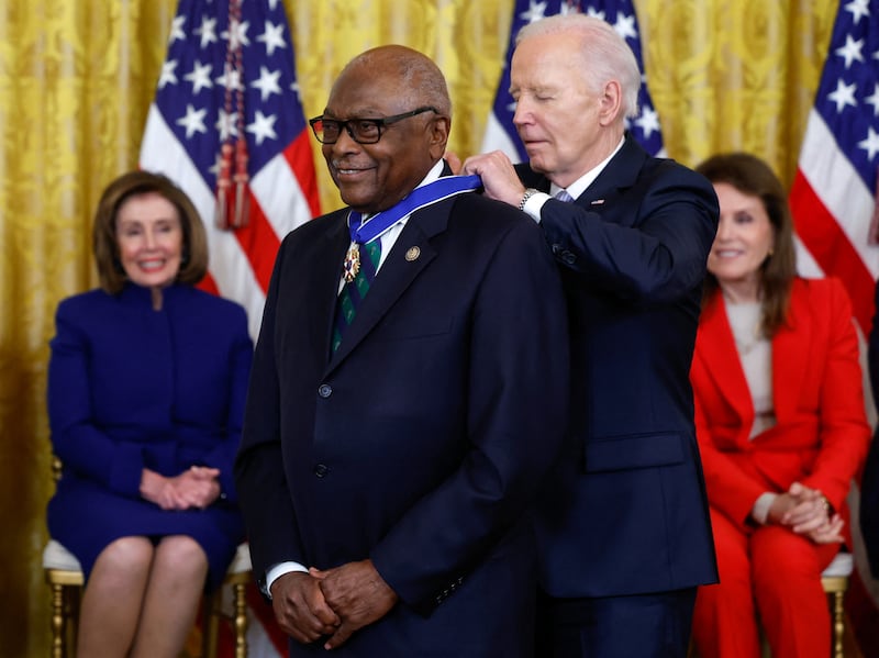 Joe Biden fastens a Medal of Freedom around James Clyburn watched by a smiling Nancy Pelosi