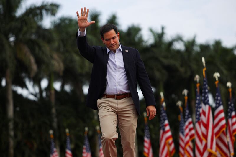 Marco Rubio raises his hand and stoops his head while walking on stage.