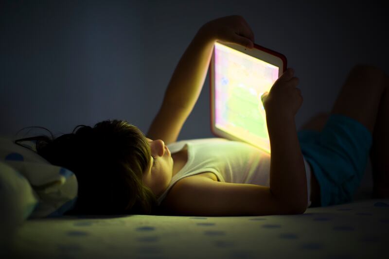 A child laying on bed staring into an iPad