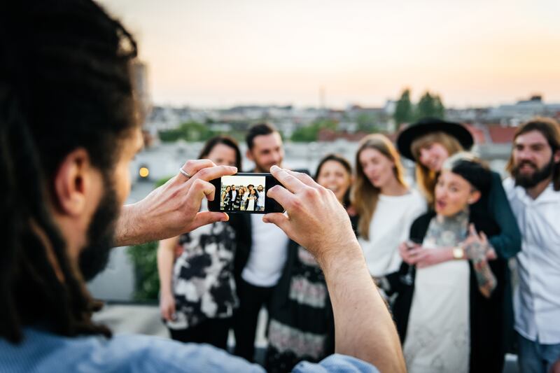 "Young man taking pictures of friends with his smart phone on the roof top"