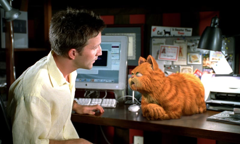 Breckin Meyer sits at a desk while Garfield lounges nearby in a still from ‘Garfield: The Movie’