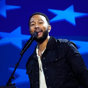 John Legend stands at a microphone, a bright blue backdrop of lighter blue stars behind him