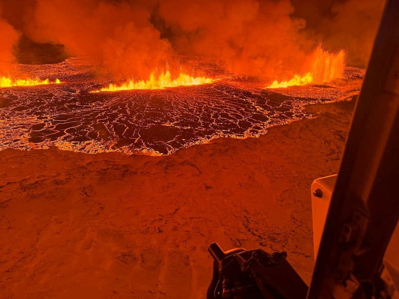 A helicopter flies near a volcano spewing lava and smoke as it erupts in Iceland.