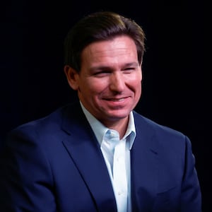 Florida Gov. Ron DeSantis smiles in a darkly lit room