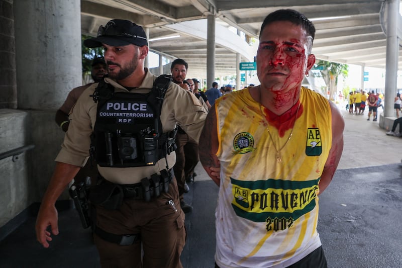 A bloodied soccer fan is detained by a police officer 