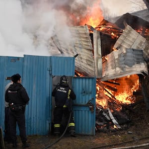 Emergency personnel work to put out a fire before a blue building.