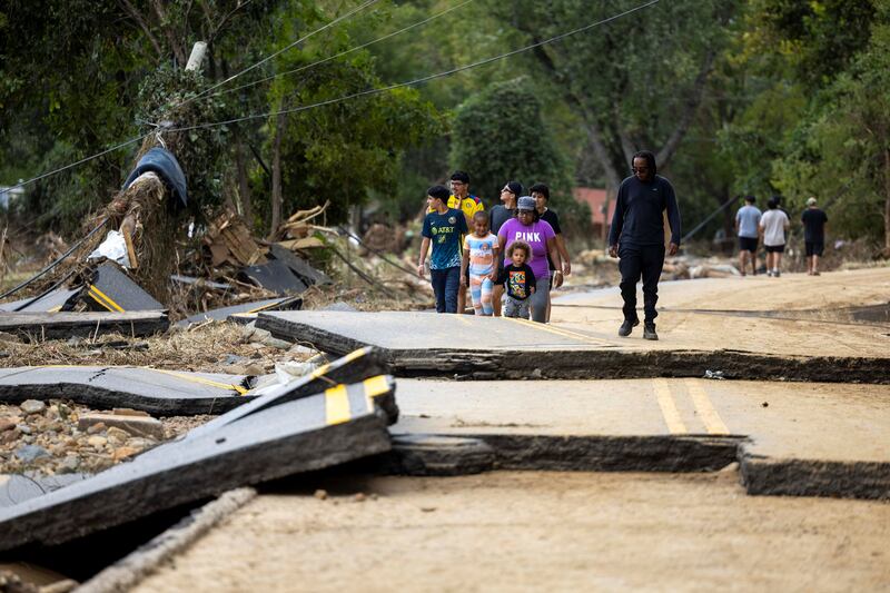 People walk across a severely damaged road.