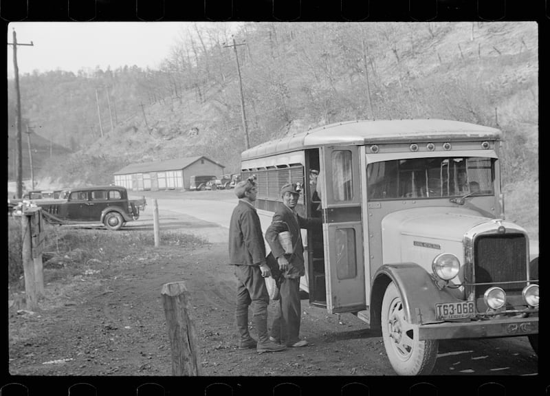 Black and white photo of coal miners getting on a bus in a mountain setting in the 1930s