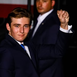 Barron Trump fist pumps while standing and wearing a blue suit, white shirt and blue tie