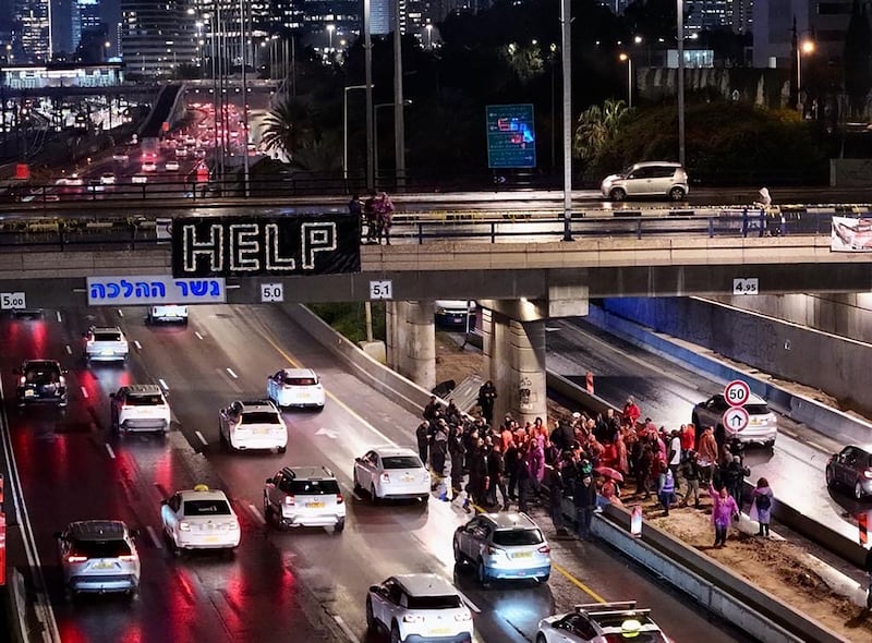 Protestors gather on a highway. A help flag can be seen thrown off an overpass.