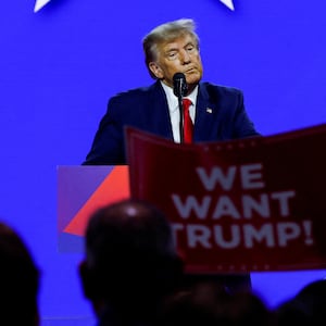 Donald Trump speaks at a conference while an audience members holds a sign that reads, “WE WANT TRUMP!”