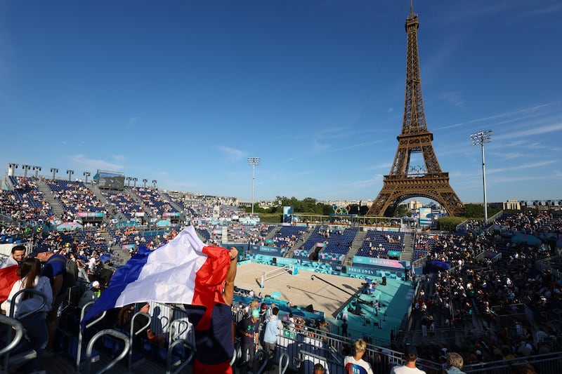 The Eiffel Tower Stadium with a beach volleyball stadium in front packed spectators, one wrapped in a French flag.