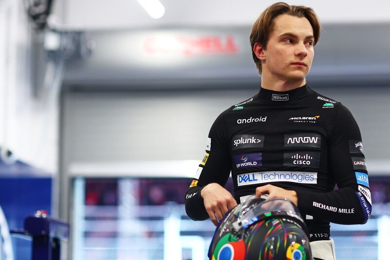 Oscar Piastri stands holding his race driving helmet