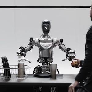 A robot sits at a table with a human standing in front of it