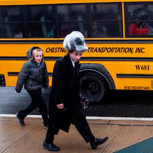 photo of two boys walking next to a school bus in a jewish neighborhood in monsey rockland county new york measles outbreak anti vax antivax rockland country de blasio forced vaccination del bigtree lawrence palevsky andrew wakefield williamsburg orthodox