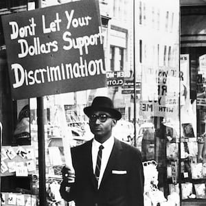 A photo including a Picketer demanding an end to lunch counter segregation made their first appearance outside a Woolworth store in Lynchburg, Virginia.