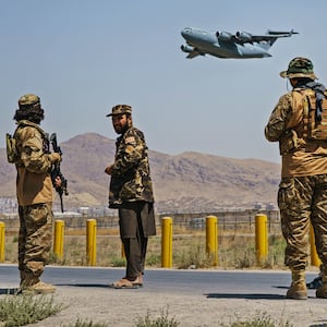 A photo of Taliban soldiers patrolling a street while a US aircraft flies off in the distance