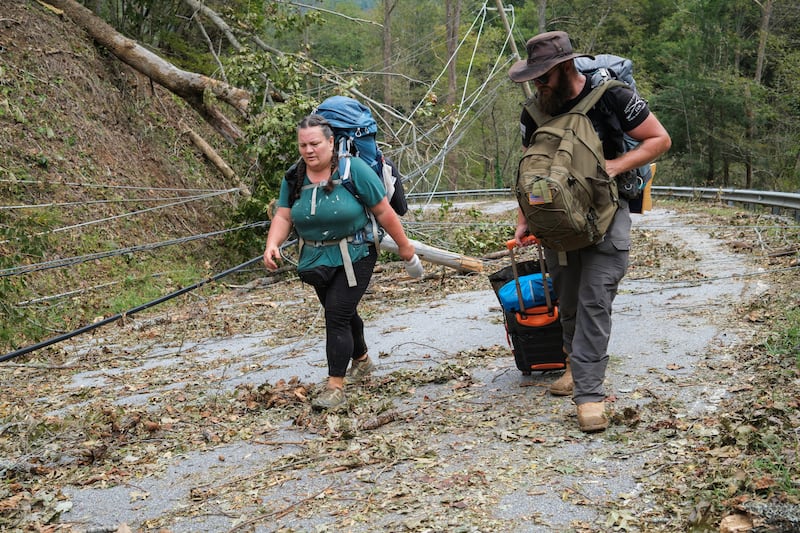 Two people walk on a damaged road with their luggage in tow.