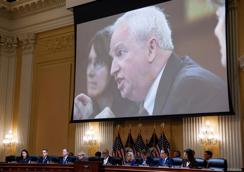 Members of the U.S. House Select Committee investigating the January 6 Attack on the U.S. Capitol sit beneath an image showing Chapman University law professor John Eastman as they hold their final meeting to release their report on December 19, 2022.