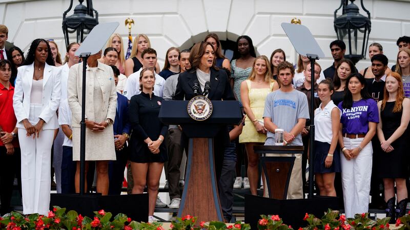 A photograph of Vice President Kamala Harris surrounded by young student athletes at the White House South Lawn. 