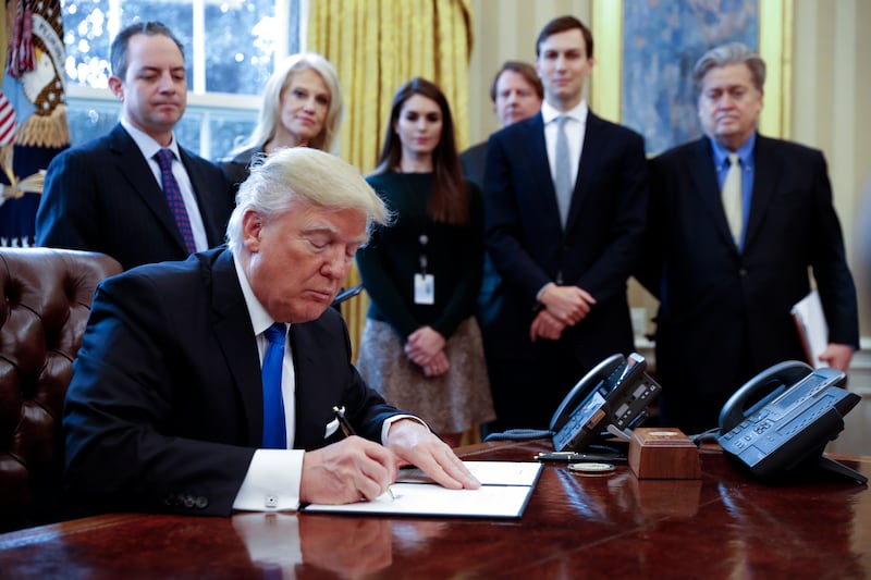 Reince Priebus, Kellyanne Conway and, to the right, Steve Bannon watch on as Trump signs an Executive Order in the Oval Office in January 2017.